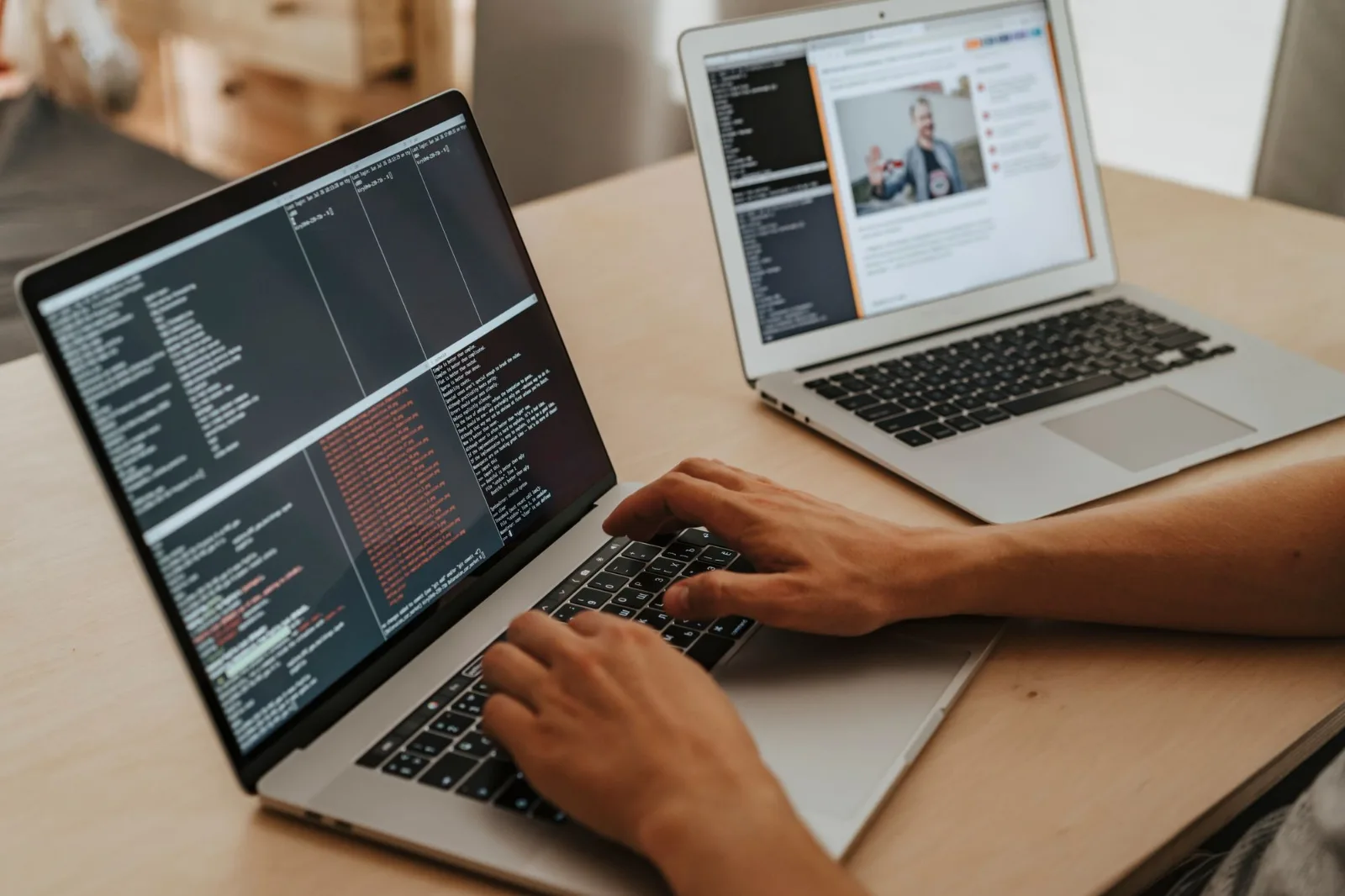 Mains sur le clavier d'un ordinateur portable affichant du code, un second portable ouvert à côté sur un bureau en bois